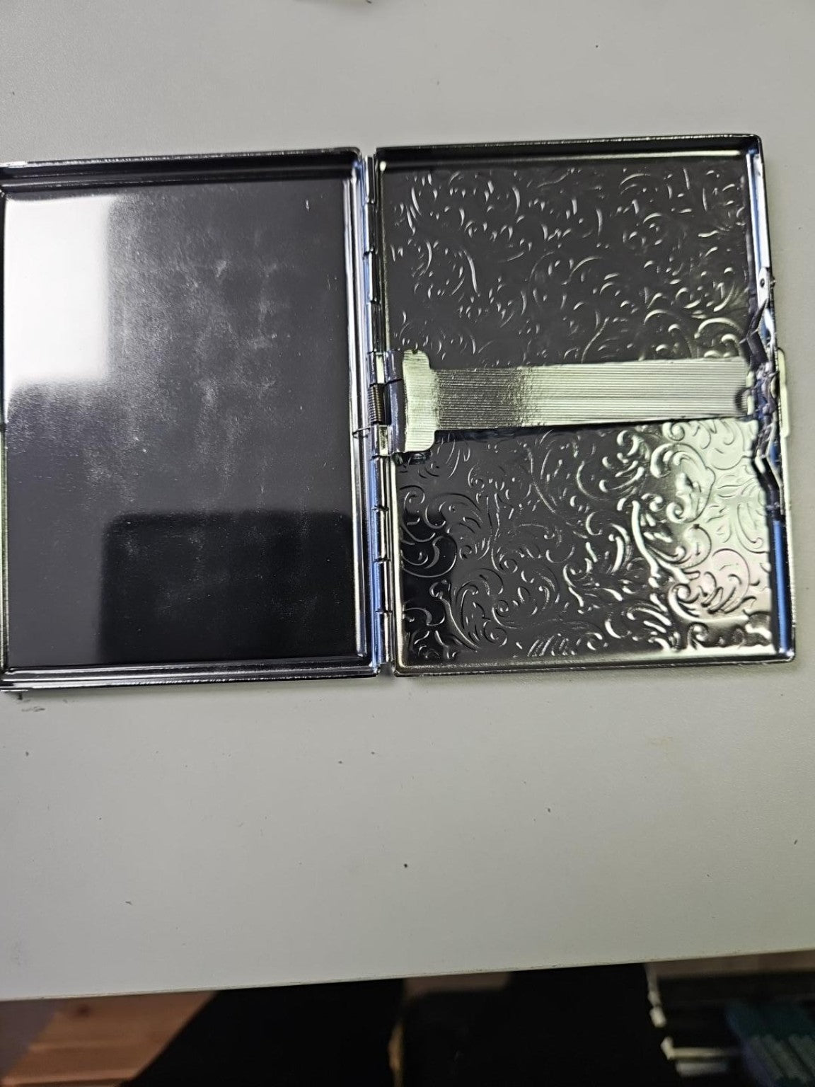 Open silver metal business card holder showing patterned metal interior and metal card-retaining bar